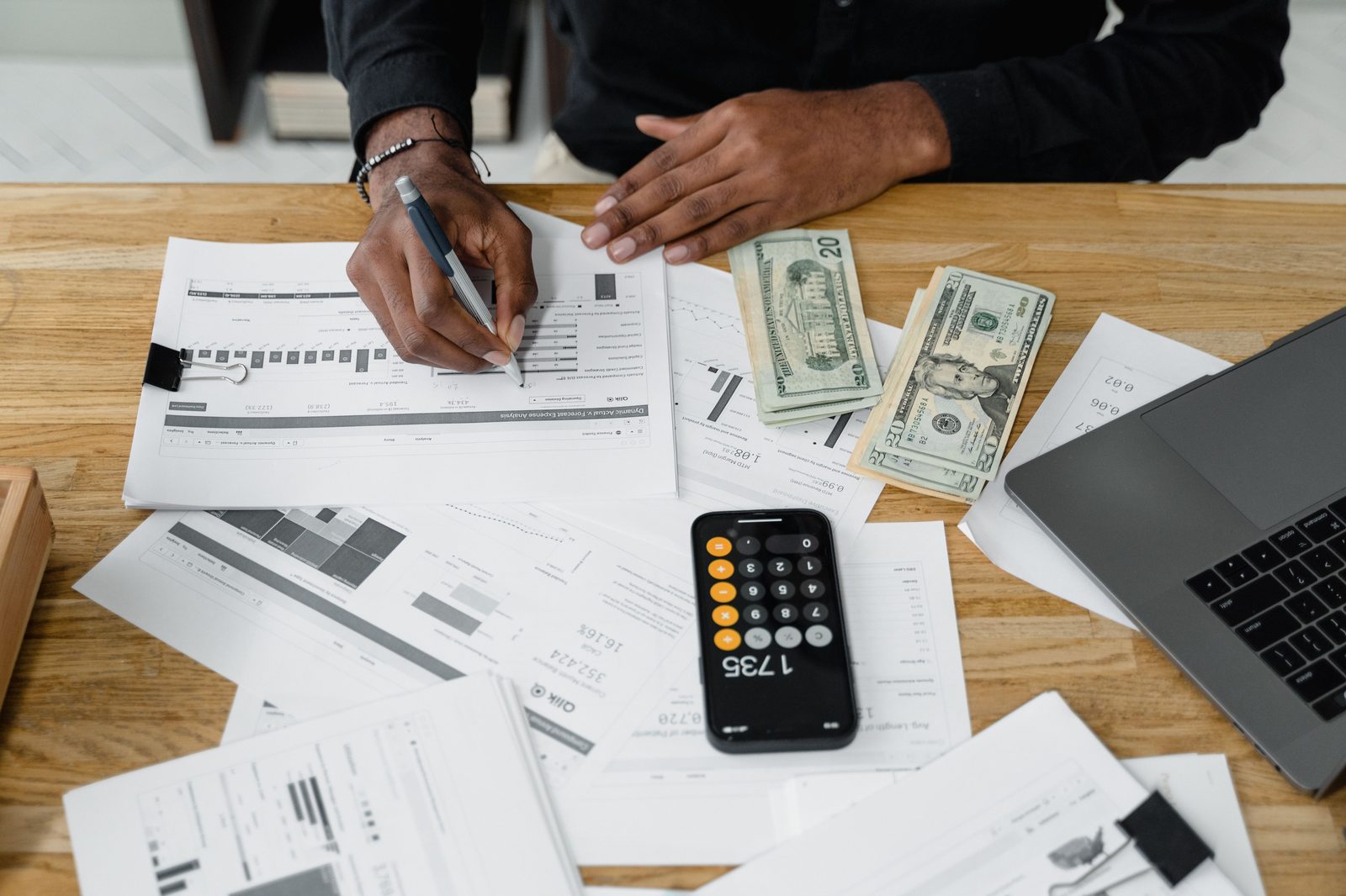Mesa de trabalho com documentos financeiros, calculadora, notas e portátil, representando o cálculo do custo de um contabilista