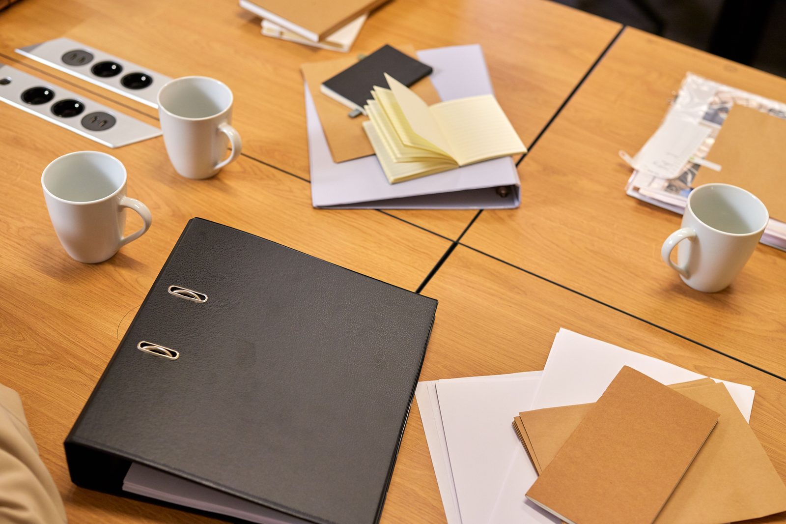 Mesa de reunião com uma pasta de arquivo, blocos de notas e chávenas de café, representando a passagem de documentação entre contabilistas