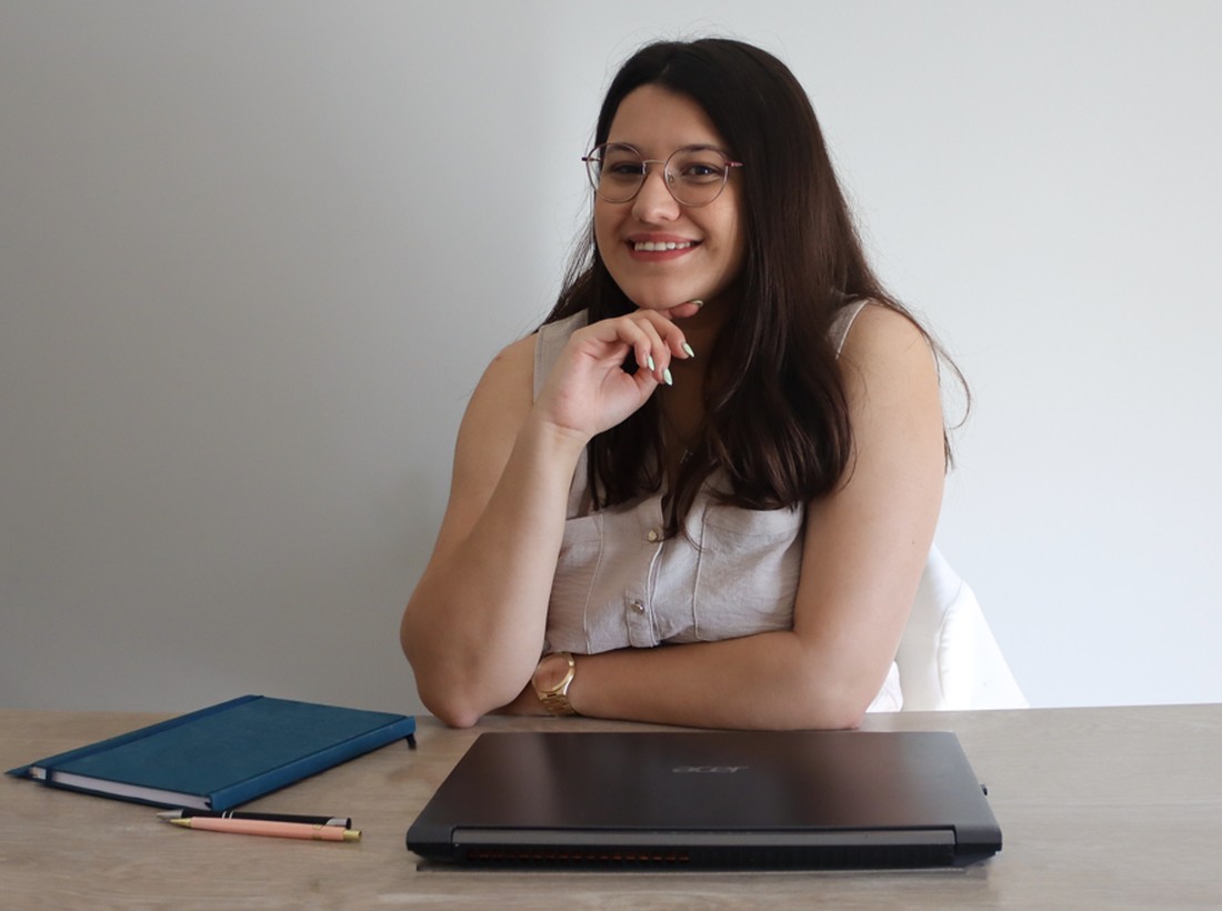 Patrícia Gonçalves a sorrir, sentada à secretária com o portátil e um caderno azul
